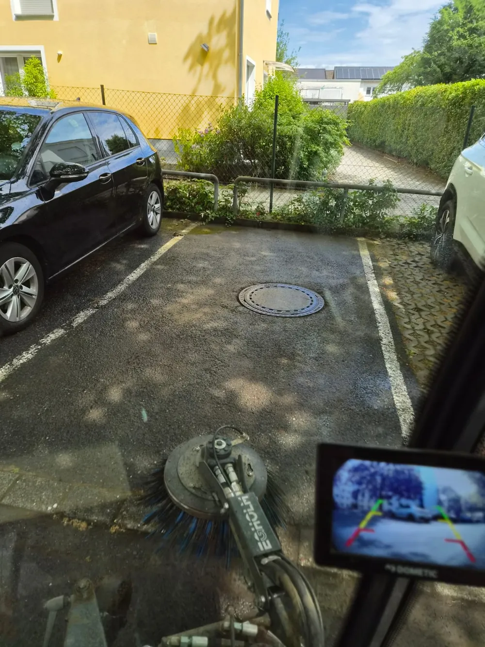 Bürste der Kehrmaschine kehrt einen Stellplatz mit Kanaldeckel