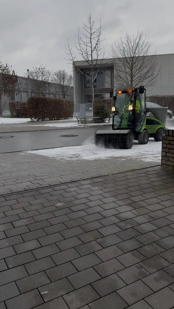 Kehrmaschine mit Schneebesen räumt einen Gehweg