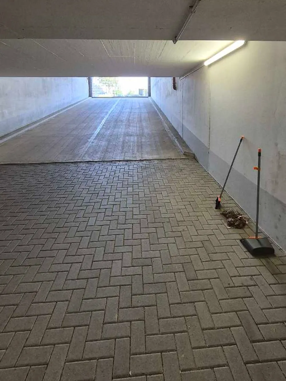 Tiefgarage mit Rohren an der Decke, Besen und zusammengekehrtem Laub
