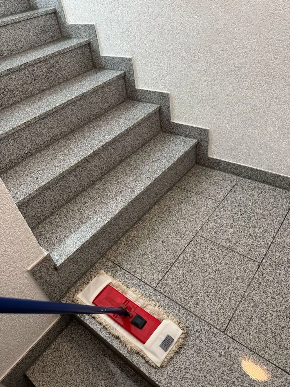 Wischmopp auf frisch gewischten Granitstufen im Treppenhaus