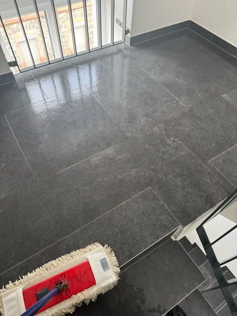 Wischmopp auf glänzendem dunklem Fliesenboden im Treppenhaus